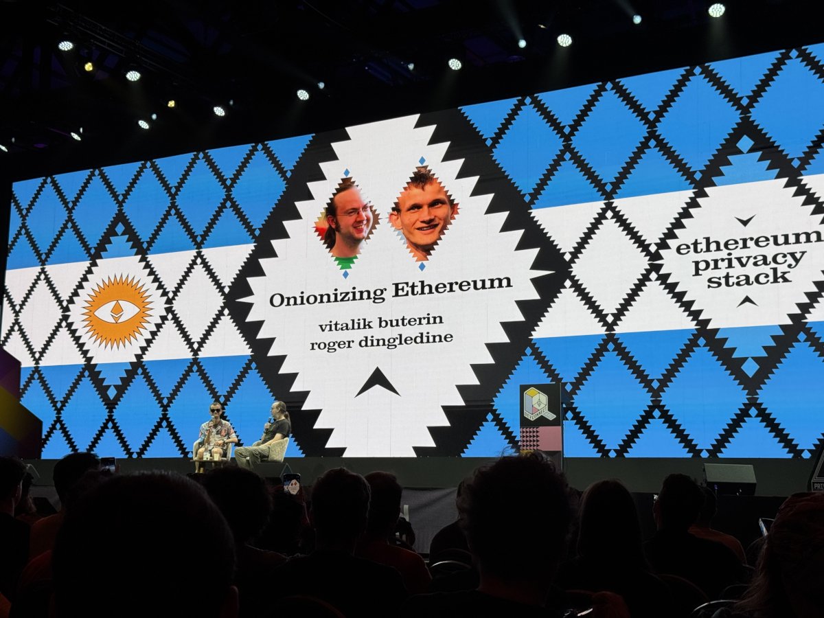 Devconnect 會場的大螢幕，寫著「Onionizing Ethereum」與講者 Vitalik Buterin、Roger Dingledine，旁邊是 Ethereum Privacy Stack 的標誌